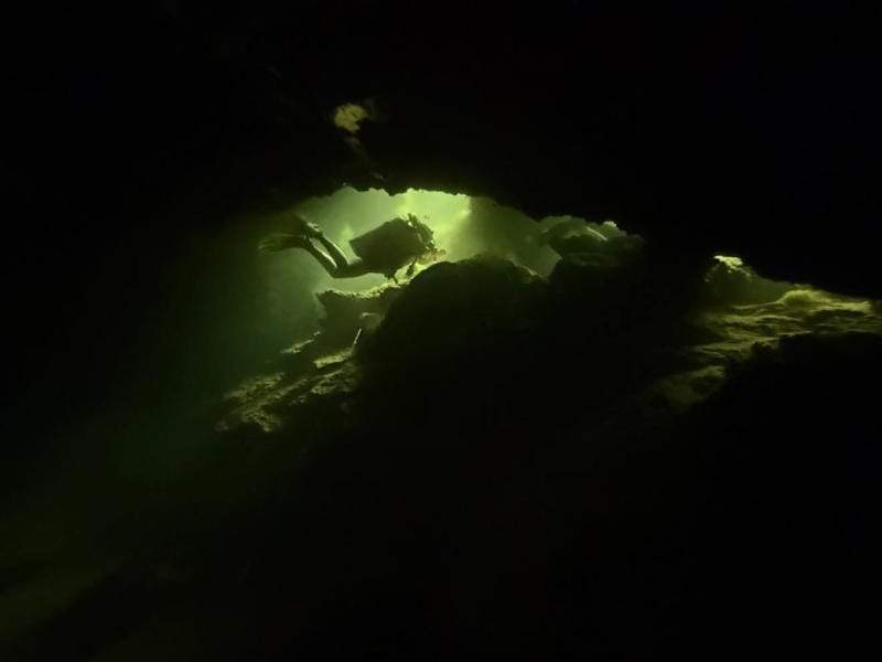 Diver floating through a dark cavern in a beam of light.